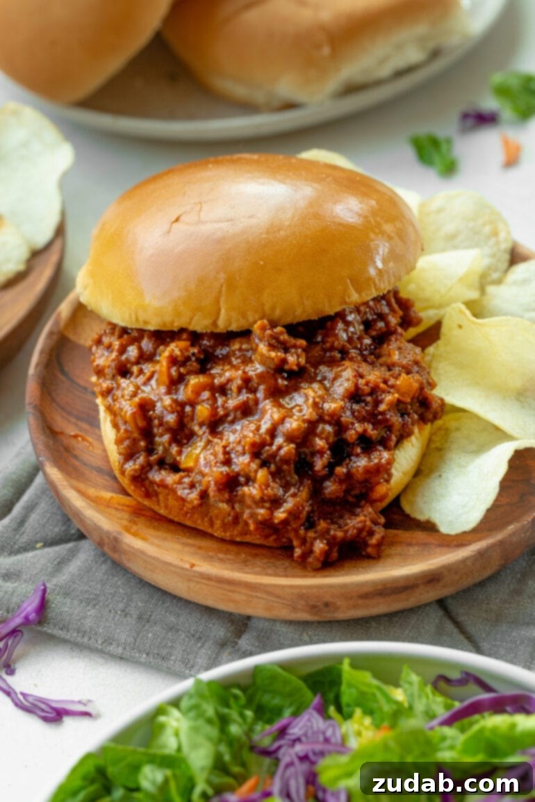 The Ultimate Sloppy Joe Recipe 8 A delectable sloppy joe sandwich resting on a rustic wooden plate, with the rich, saucy filling overflowing from the bun, accompanied by a stack of crispy potato chips.