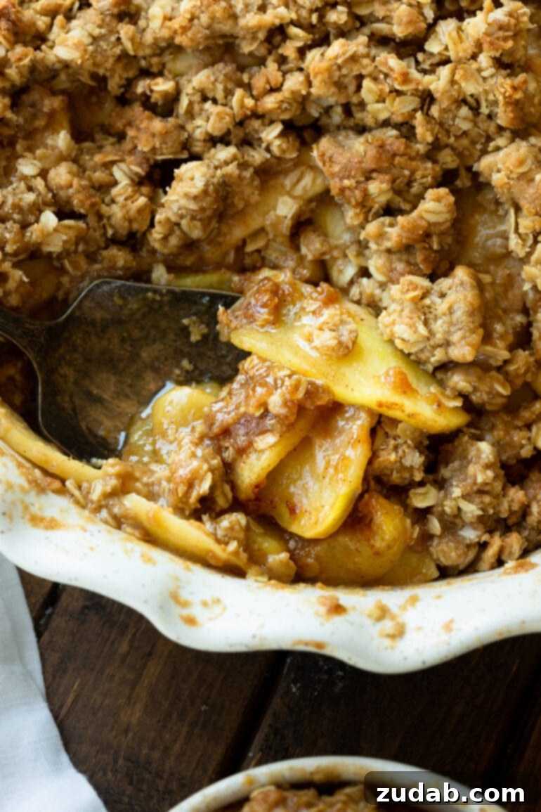 The Ultimate Homemade Apple Crisp 10 A close-up view of a homemade apple crisp, with a portion scooped out, offering a tantalizing glimpse of the perfectly tender, warmly spiced apple chunks nestled beneath the golden, crumbly oat topping. This image highlights the rich texture and inviting warmth of the dessert.