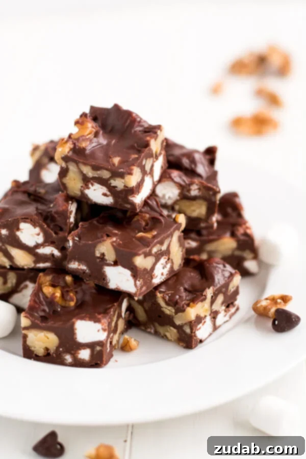 Effortlessly create delectable Rocky Road Fudge in under 10 minutes! Stacked squares of homemade Rocky Road Fudge on a white dessert plate, perfect for holidays.