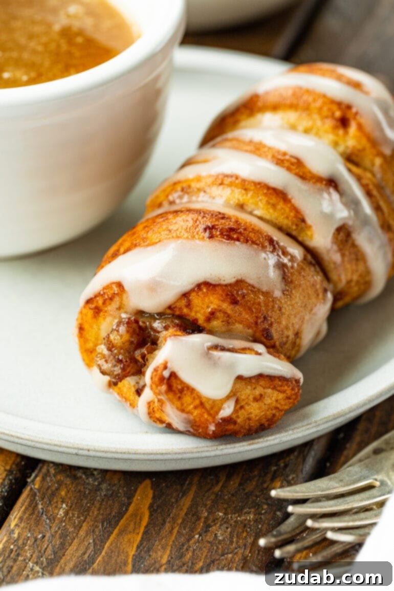 Pigs in a Sweet Blanket 7 A delightful arrangement of a cinnamon roll sausage dunker on a plate, with a small cup of maple butter sauce invitingly placed beside it. The scene captures the essence of a perfect, kid-friendly breakfast.