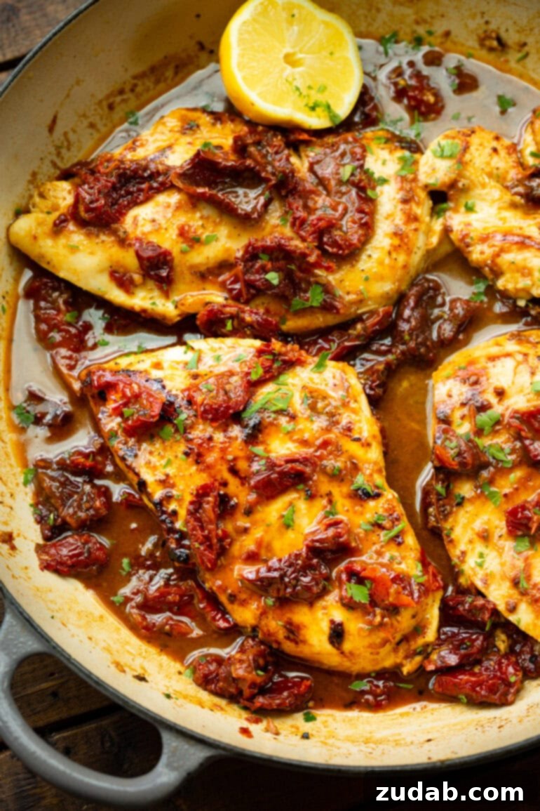 Zesty Citrus Greek Chicken 8 Several perfectly seared golden chicken breasts, generously topped with ruby-red sun-dried tomatoes, simmering in a rich, flavorful sauce within a shallow Dutch oven.