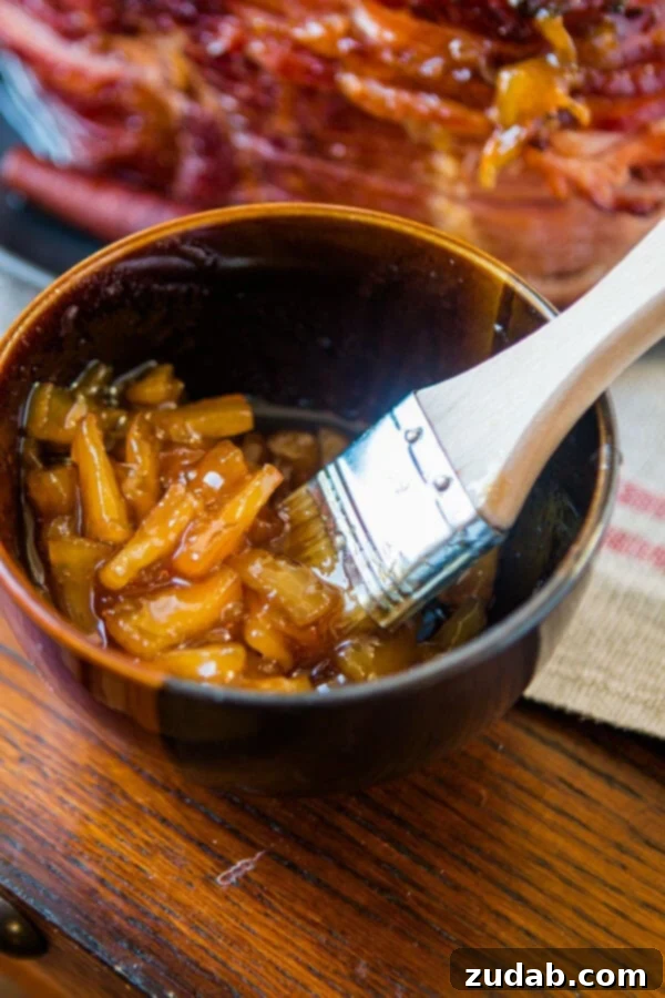 Perfecting the World's Best Brown Sugar Ham with a homemade glaze. A close-up of a brush applying a luscious brown sugar glaze onto a prepared ham, highlighting the rich, thick texture of the sauce.