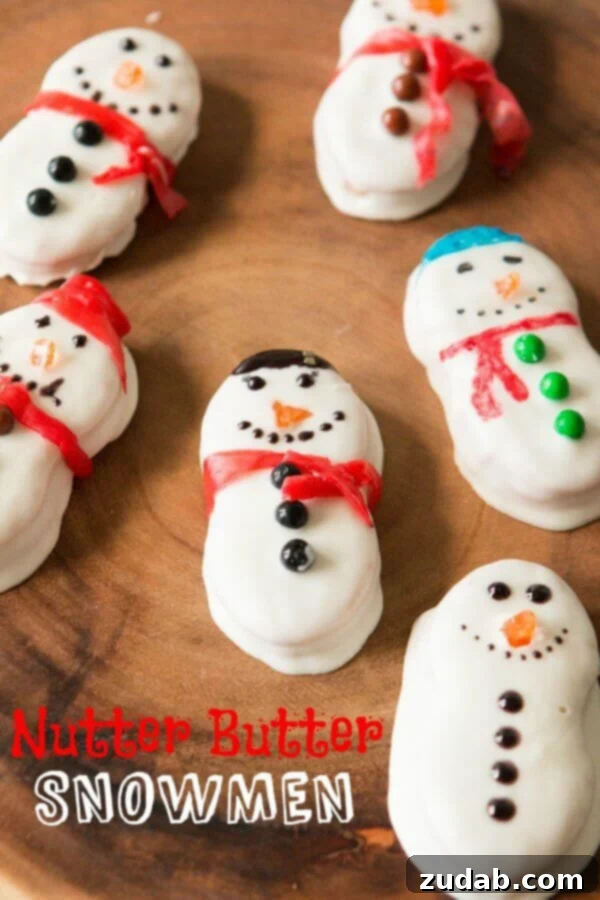 Nutter Butter Snowman Treats 2 Close-up of three finished Nutter Butter Snowmen, dipped in white chocolate with fruit roll-up scarves and decorated faces, sitting on a wooden surface.