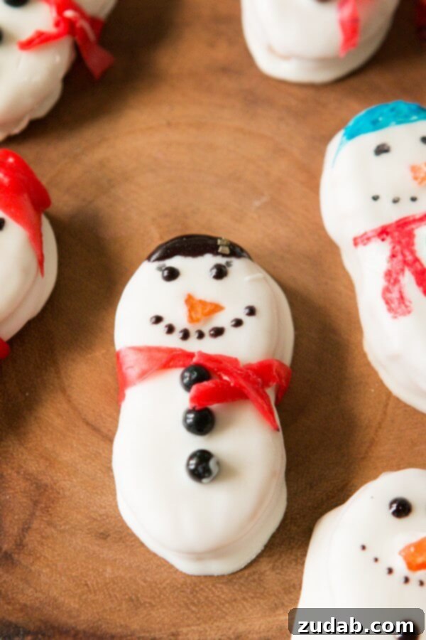 These Nutter Butter Snowmen will bring a smile to your face on a cold winter day! Dipped in white chocolate and topped with fruit roll ups, they are a festive, delicious, ADORABLE treat just in time for the class Christmas party! Christmas cookies, no-bake dessert, 5 minutes A pair of Nutter Butter Snowmen, showcasing their white chocolate coating, cheerful faces with sprinkles for eyes, and colorful fruit roll-up scarves.