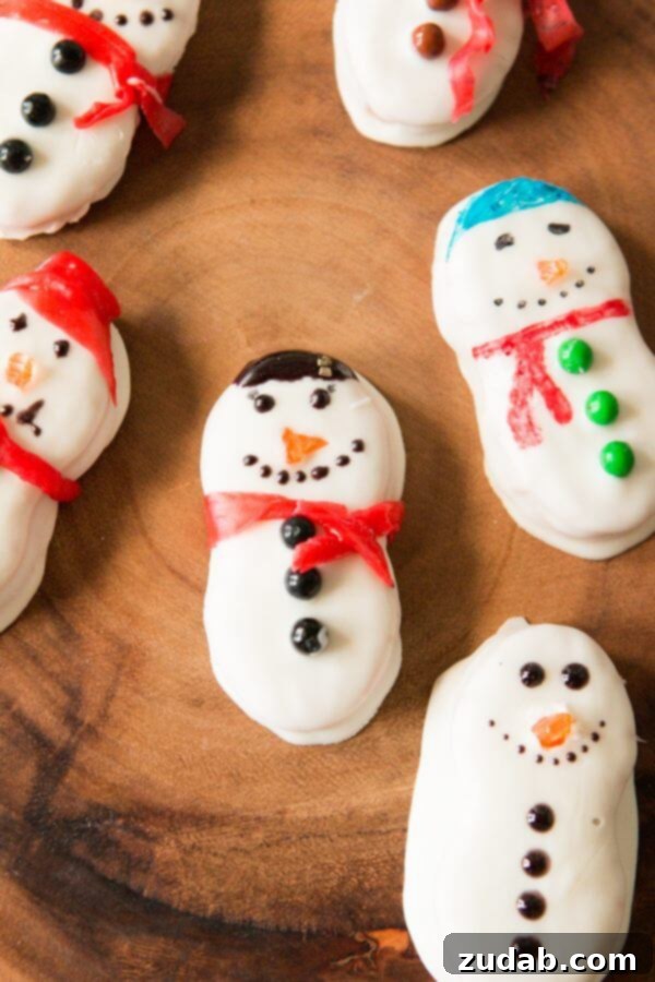 These Nutter Butter Snowmen will bring a smile to your face on a cold winter day! Dipped in white chocolate and topped with fruit roll ups, they are a festive, delicious, ADORABLE treat just in time for the class Christmas party! Christmas cookies, no-bake dessert, 5 minutes Various Nutter Butter Snowmen decorated with different fruit roll-up scarves, sprinkle eyes, and candy noses, displayed on a platter.
