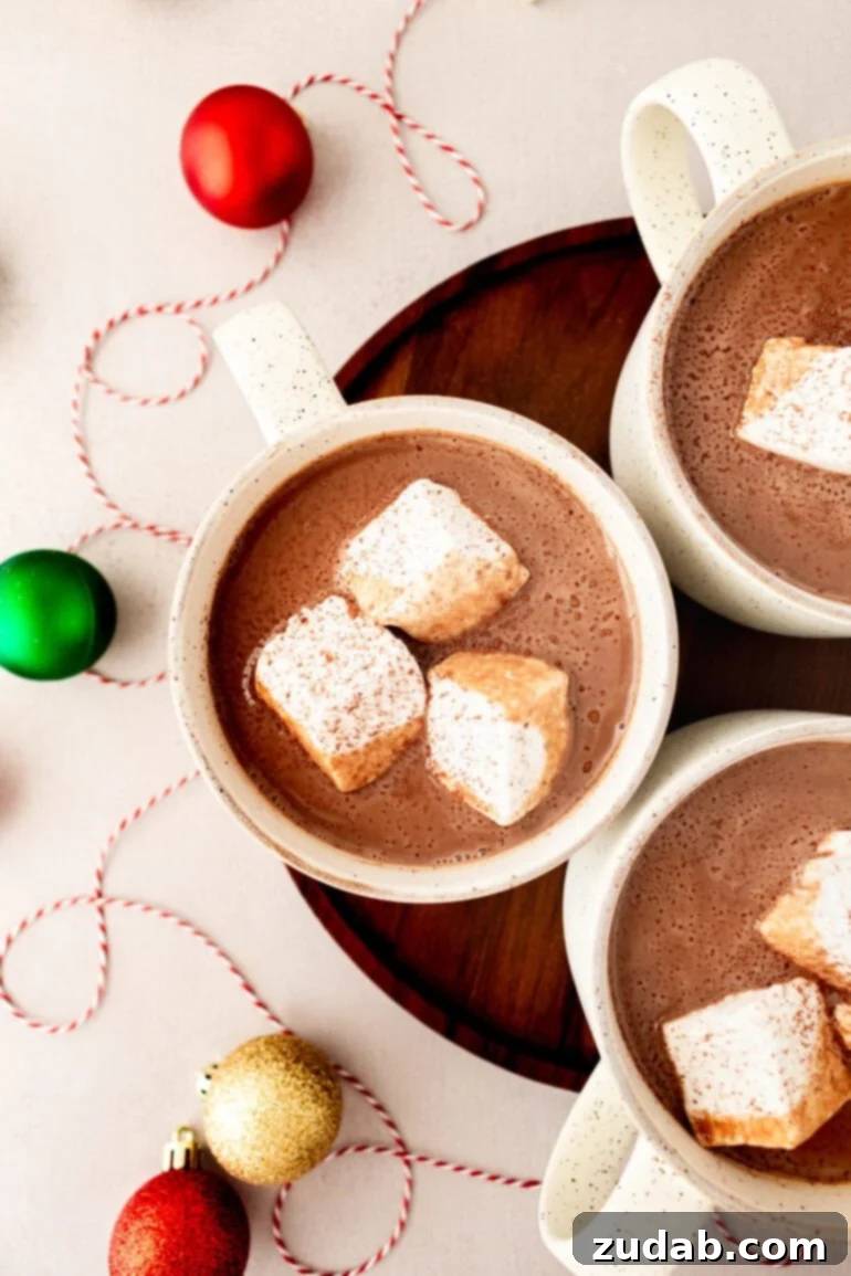 Blissful Homemade Hot Chocolate 2 A photo taken over the top of three mugs of creamy hot cocoa, each with 3 large marshmallows floating in them, inviting warmth and comfort.