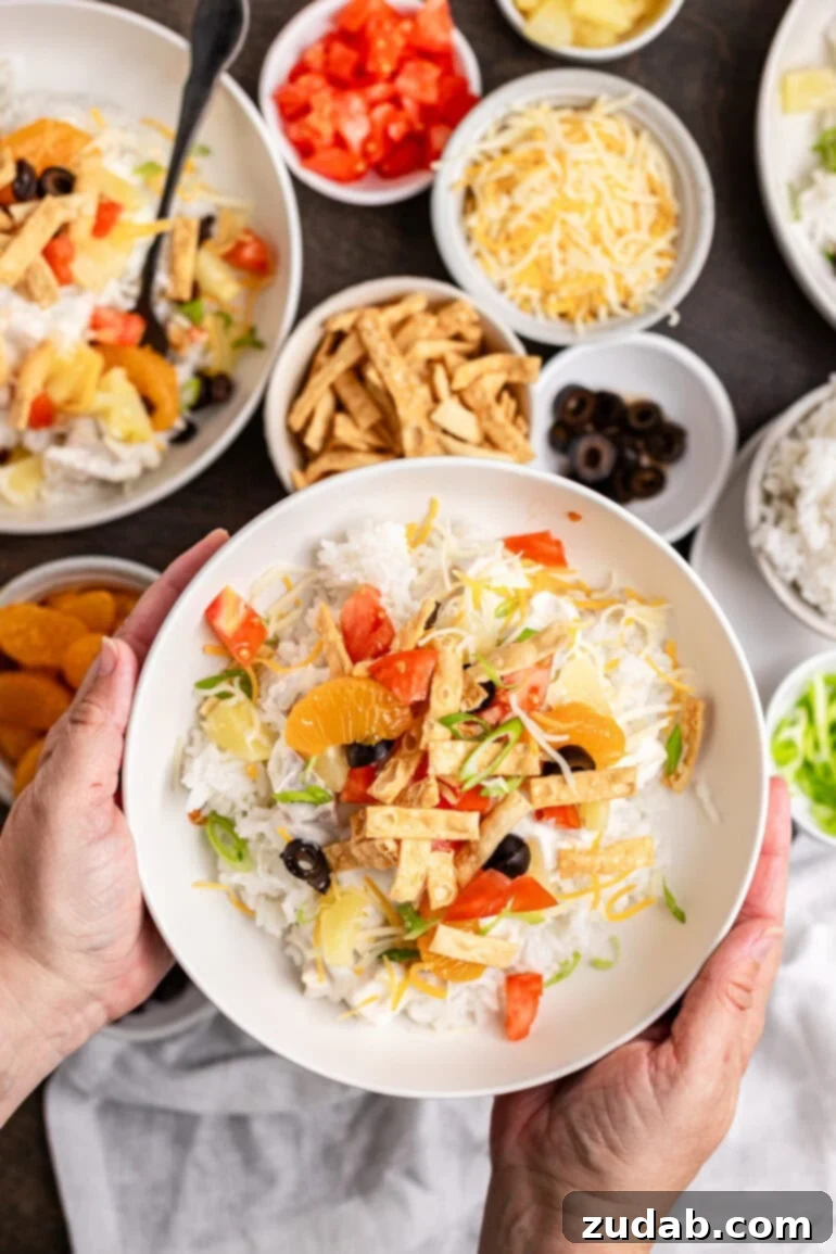 Ditch the soup cans and Chinese noodles, this is ultimate Hawaiian haystacks recipe and you're going to go crazy for them! A white bowl filled with Hawaiian Haystacks topped with pineapple chunks, cheddar cheese, green onions, and fresh tomatoes.