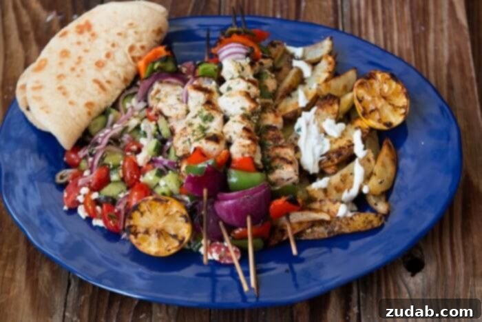 Looking for an easy and delicious chicken for the grill? Greek Chicken Souvlaki is full of flavor and turns out so moist! A large blue platter featuring chicken souvlaki kabobs, a fresh Greek salad, and warm pita bread.