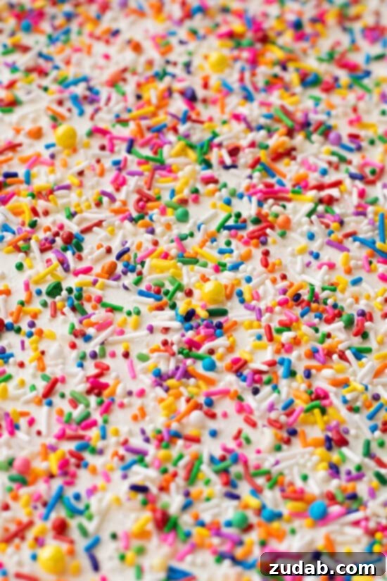 Close-up of Homemade Funfetti Cake slice, showing colorful sprinkles inside and creamy frosting.