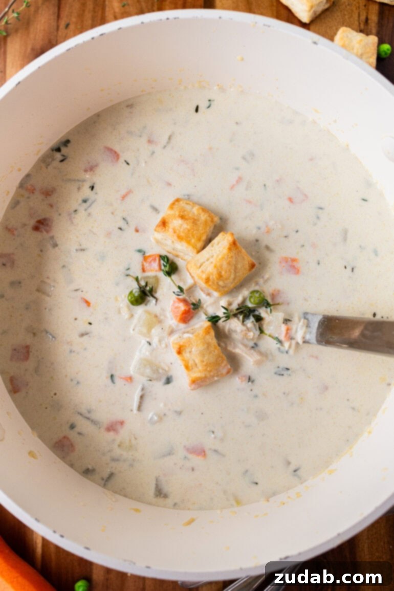 Velvety Chicken Pot Pie Soup 11 A photo of a bowl of creamy chicken pot pie soup topped with mini biscuits with a spoon sitting in the bowl, ready to eat.