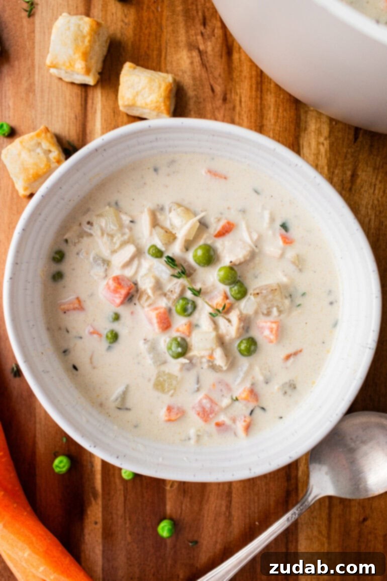 Velvety Chicken Pot Pie Soup 4 A photo of a bowl of creamy chicken pot pie soup in a white bowl sitting on a wooden table, garnished with fresh herbs.