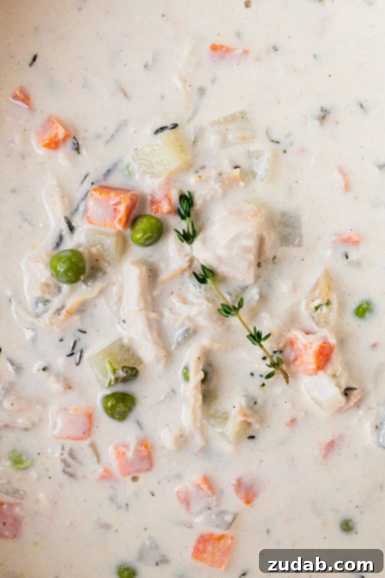 Velvety Chicken Pot Pie Soup 10 A close-up photo of creamy chicken pot pie soup with visible chunks of chicken, peas, carrots, and fresh herbs, emphasizing its hearty nature.