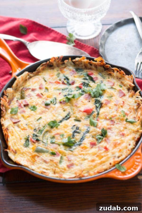 Golden hash browns make a great crust for this hash browns ham frittata! Serve as is or with hot sauce for a spicy little pop! low-carb Delicious hash browns ham frittata with a crispy crust, served on a white plate with fresh parsley garnish.