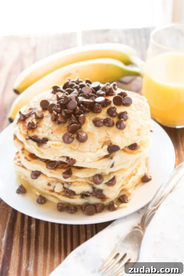 Better Than Mom's Chocolate Chip Pancakes Stack of golden-brown chocolate chip pancakes on a white plate, with fresh banana slices and orange juice in the background, highlighting a perfect breakfast scene.
