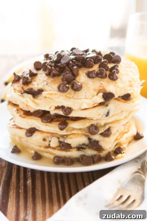 Better Than Mom's Chocolate Chip Pancakes Close-up shot of a stack of chocolate chip pancakes on a white plate, with a fork and napkin next to it, inviting a delicious bite.