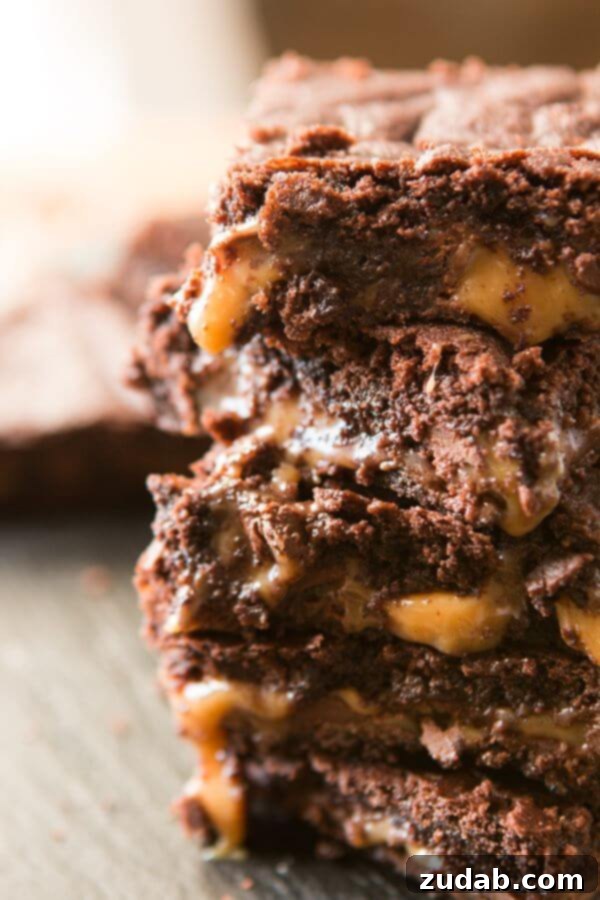 A tall stack of rich, gooey Caramel Brownies Made from Scratch, glistening with chocolate and caramel
