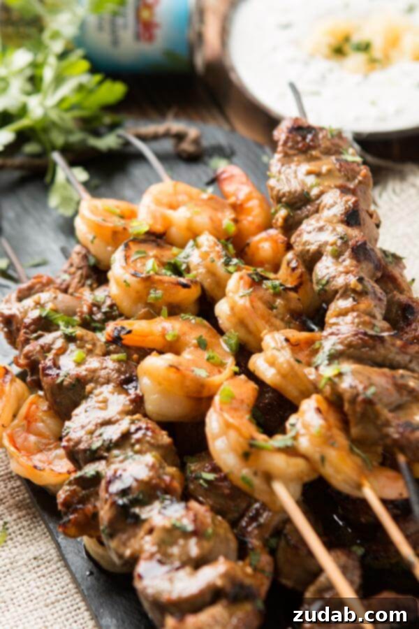 Grilled spicy steak and shrimp kabobs with a side of creamy pina colada sauce, perfect for summer barbecues.