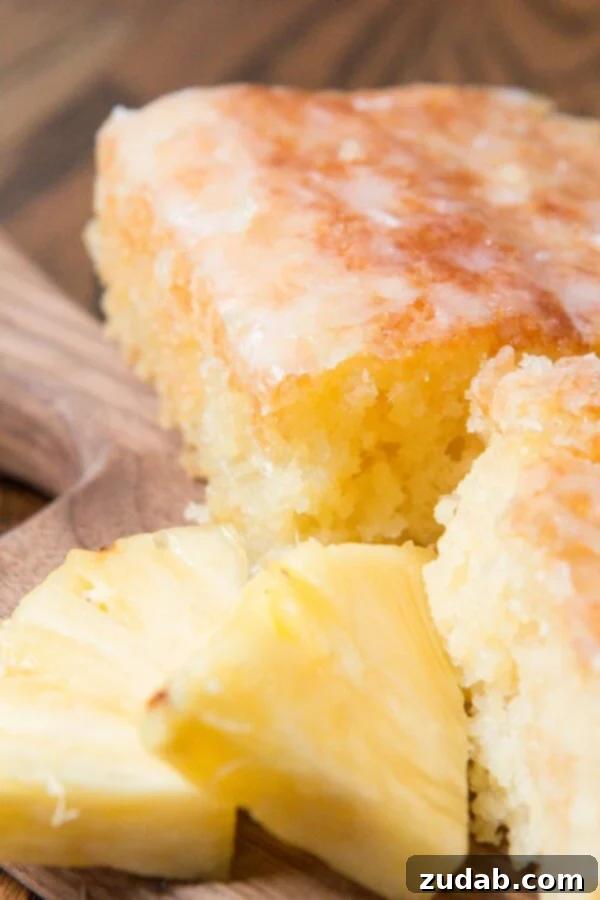Pineapple crush jello cake is seriously one of the most moist cakes out there. The pineapple niblets are barely noticeable but give such flavor! A close-up, angled shot of two moist slices of Island-Inspired Jello Pineapple Cake, generously topped with a creamy coconut glaze and artfully arranged with chunks of fresh pineapple, evoking a tropical paradise.