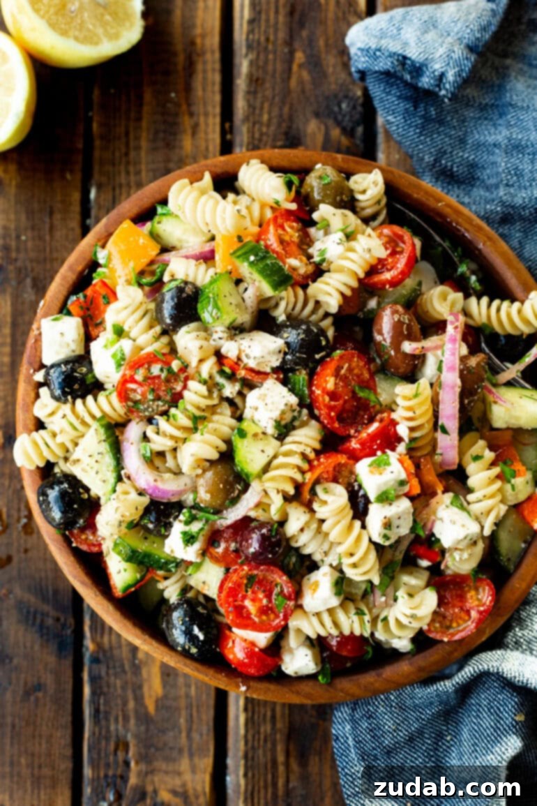 Greek Isles Pasta Salad 5 a photo taken over the top of a large wooden serving bowl full of greek pasta salad including tomatoes, red onions, black olives, cucumber, feta cheese and rotini pasta