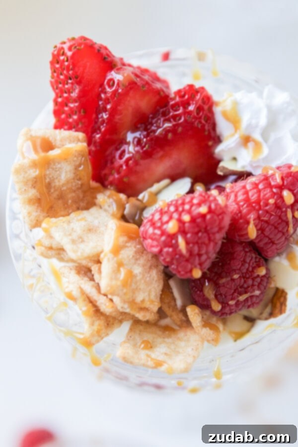 Two hands hold up a glass of Cinnamon Berry Crisp Yogurt Parfait, a delicious and easy breakfast idea from Oh Sweet Basil.