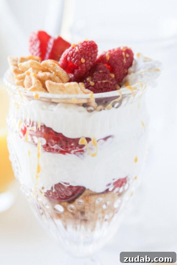 Fresh berries and Mom's Best Cereal Toasted Cinnamon Squares are stacked next to a bowl of creamy Greek yogurt, ready for a healthy parfait.
