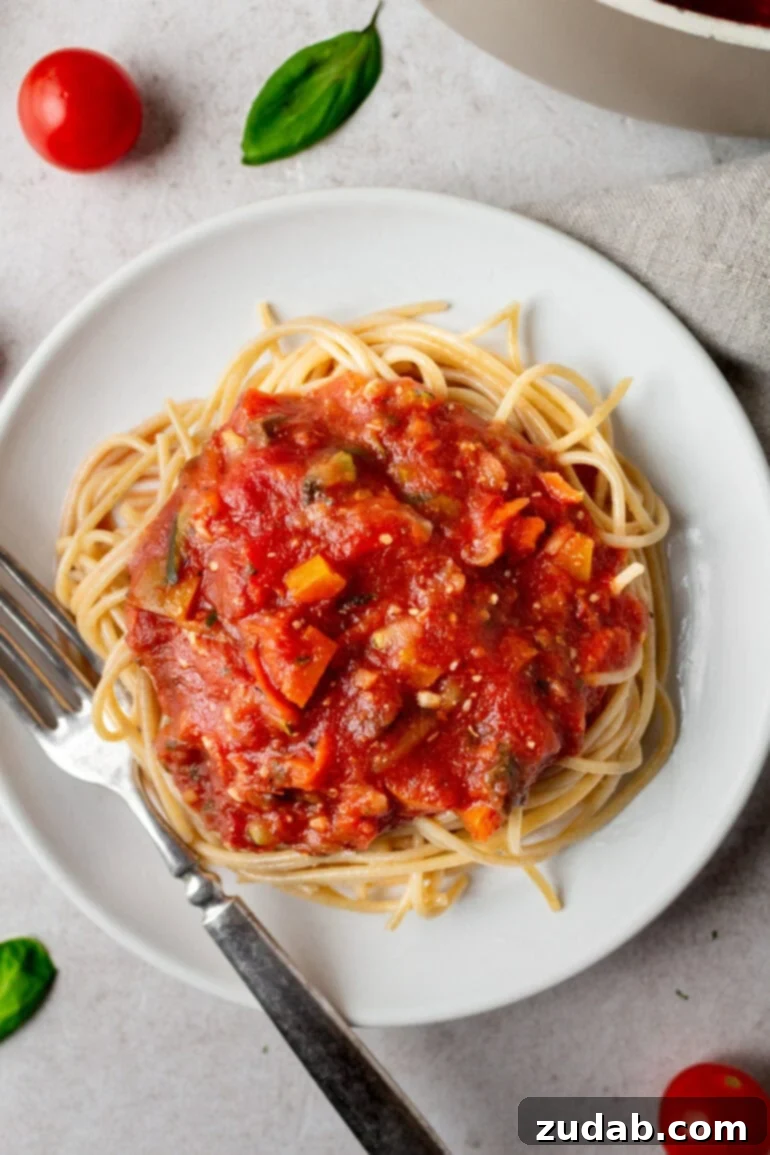 Garden-Fresh Homemade Marinara Sauce 2 A vibrant photo of garden veggie marinara sauce generously spooned over a bed of cooked angel hair pasta, garnished with fresh basil.