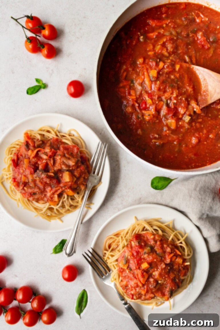 Garden-Fresh Homemade Marinara Sauce 4 A beautifully composed shot showing a pot of simmering veggie marinara sauce, with two plates of angel hair pasta topped generously with the delicious sauce.