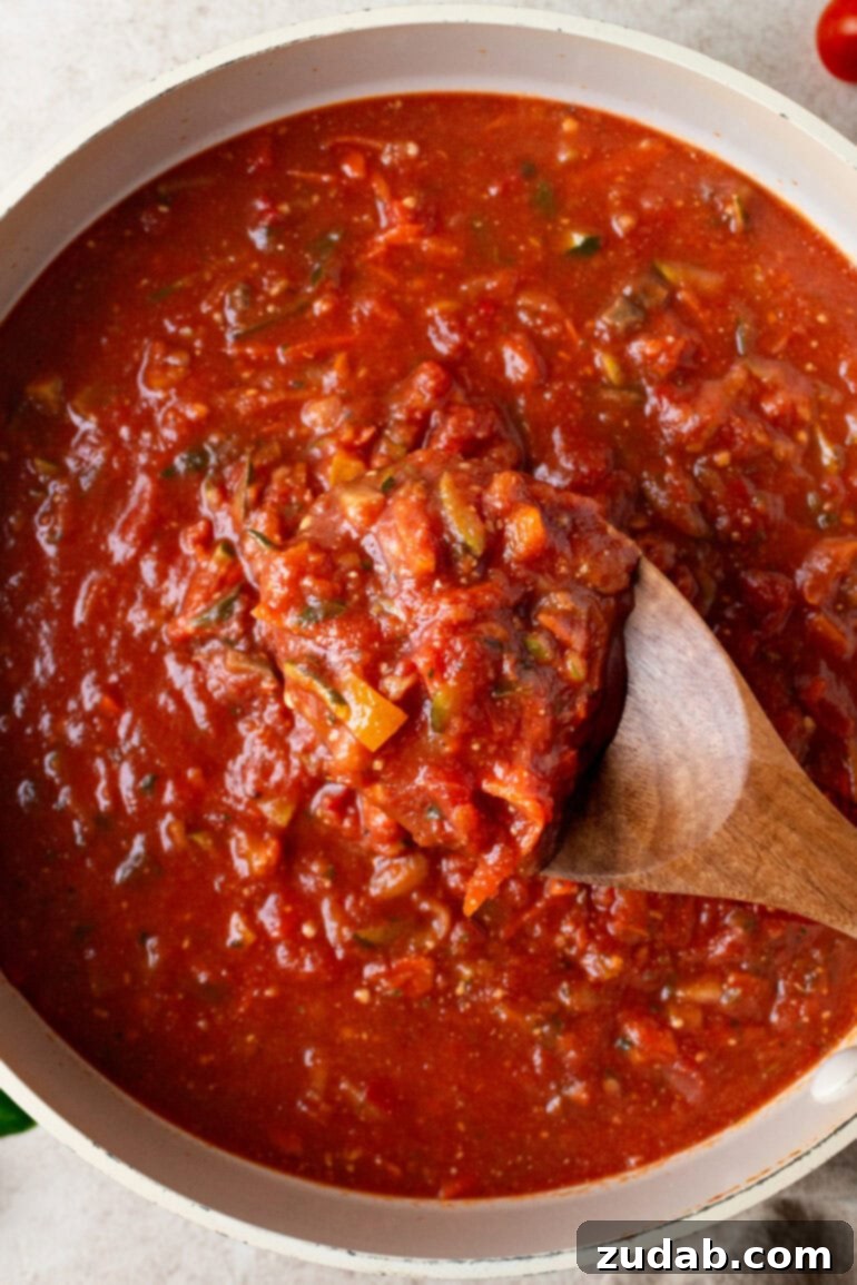 Garden-Fresh Homemade Marinara Sauce 8 A wooden spoon lifting a generous spoonful of steaming vegetable marinara sauce out of a large, rustic pot, ready to be served.