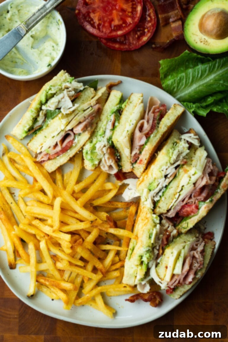 The Ultimate Triple Decker Club Sandwich 4 a photo of a triple decker club sandwich that has been cut into quarters laying on a white place next to a serving of crispy golden fries.