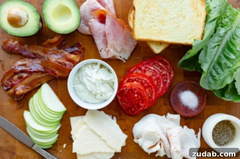 The Ultimate Triple Decker Club Sandwich 5 a photo of all the ingredients for a club sandwich including white bread, tomato slices, turkey, ham, crispy bacon, avocado, cheese and granny smith apples.