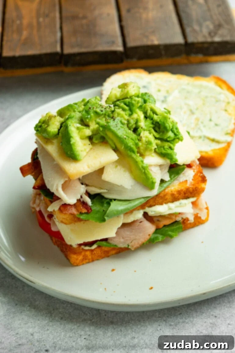 The Ultimate Triple Decker Club Sandwich 7 a photo of a club sandwich with the top slice of bread removed showing the sandwich topped with slices of avocado and cheese.