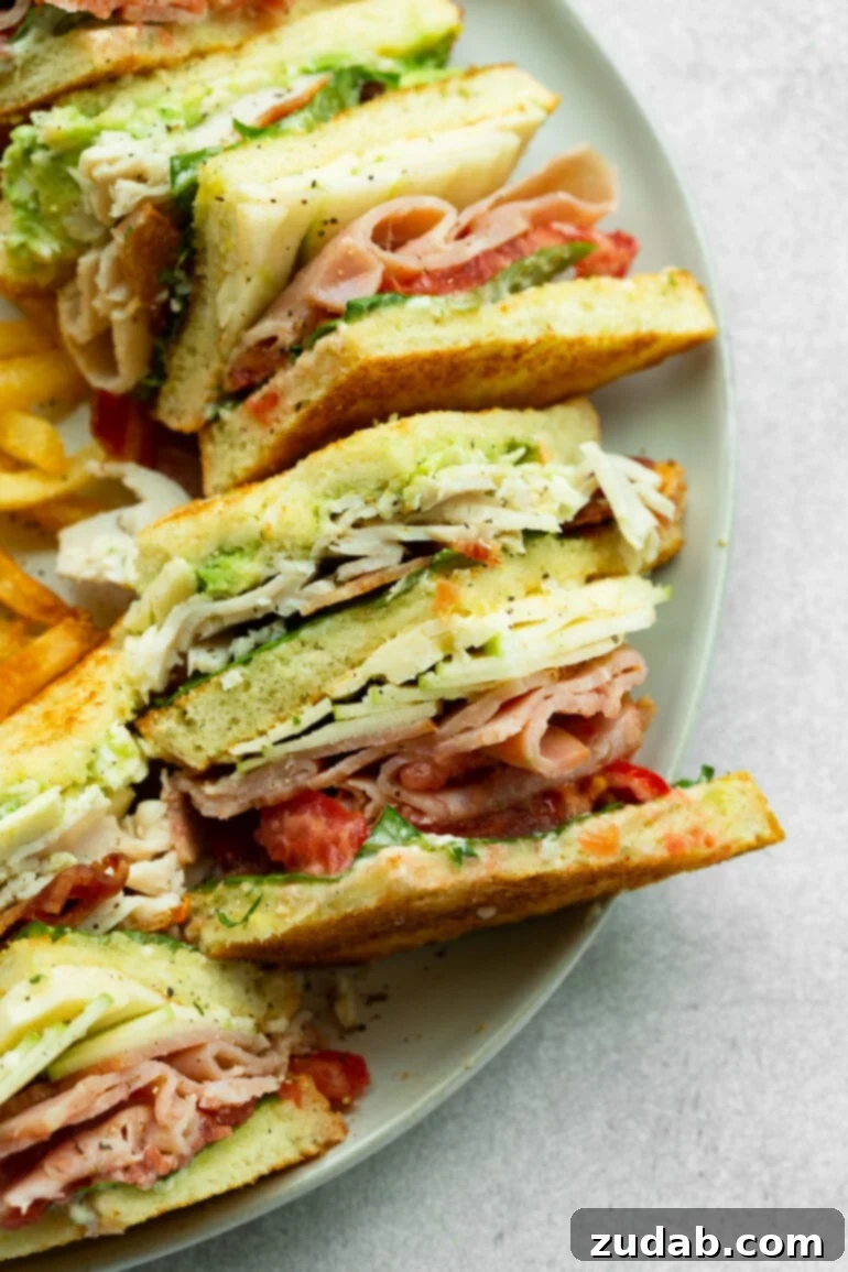 The Ultimate Triple Decker Club Sandwich 8 a photo of a section of a triple decker club sandwich laying on its side showing all the layers including turkey, bacon, tomatoes, lettuce, avocado and cheese.