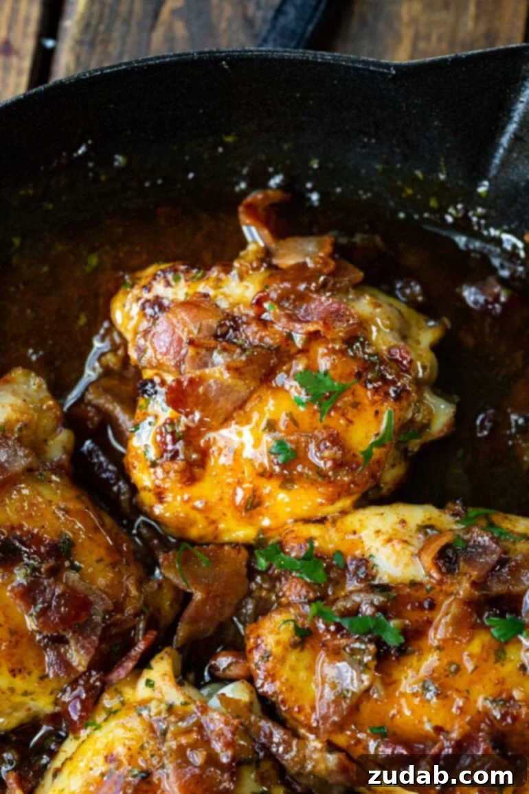 A photo of a golden chicken thigh nestled in a rich, glossy honey mustard sauce within a cast iron skillet, garnished with fresh herbs.