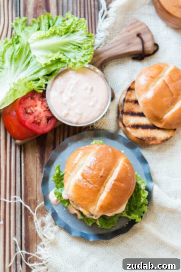 The Ultimate Burger Experience: Homemade Sauce and Perfect Toppings An overhead view of a beautifully assembled cheeseburger, sauce generously flowing from the sides, accompanied by a perfectly grilled bun, a small bowl of the signature sauce, and freshly sliced tomatoes.