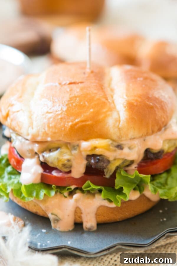 Homemade Killer Burger Sauce: The Ultimate Flavor Enhancer for Your Grilling Season A striking side-view photograph of a thick, juicy cheeseburger, featuring crisp lettuce, a vibrant tomato slice, and a generous cascade of creamy homemade burger sauce.
