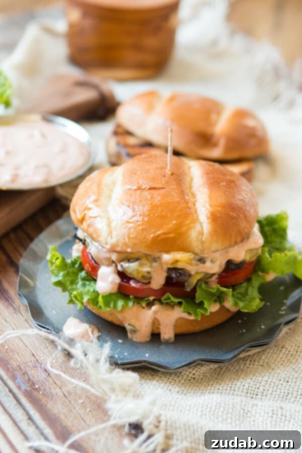 The Essential Homemade Killer Burger Sauce for Every Burger Lover A mouth-watering view of a thick, juicy cheeseburger generously layered with crisp lettuce, fresh tomato slices, and a rich burger sauce cascading down its sides, nestled in a soft bun.