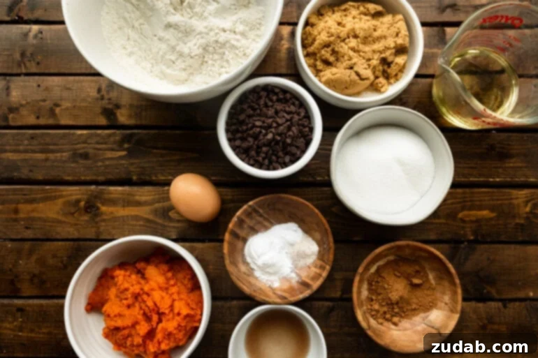 The Ultimate Pumpkin Chocolate Chip Cookies 4 A photo displaying all the ingredients for pumpkin chocolate chip cookies neatly arranged in separate small bowls, including brown sugar, flour, various spices, pumpkin puree, chocolate chips, and an egg.
