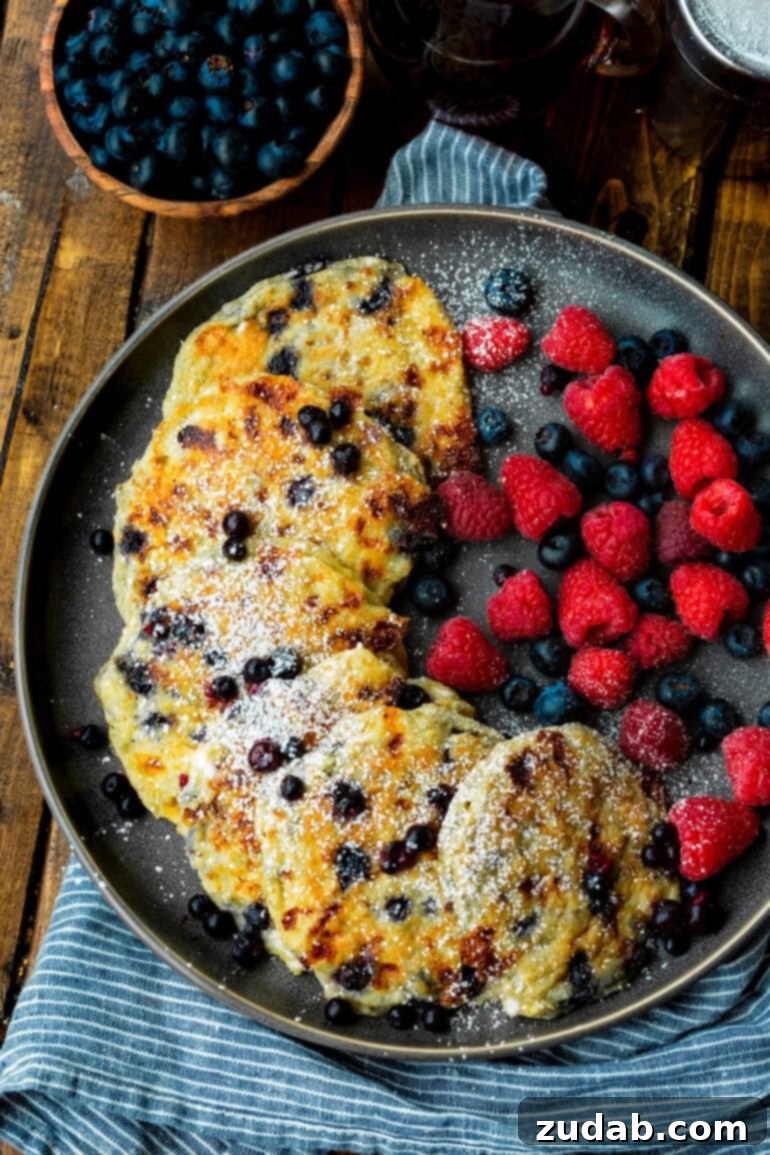 Protein-Packed Wild Blueberry Cottage Cheese Pancakes 7 A photo showcasing several golden blueberry pancakes arranged on a plate, accompanied by fresh blueberries and raspberries on the side, inviting a delightful breakfast experience.