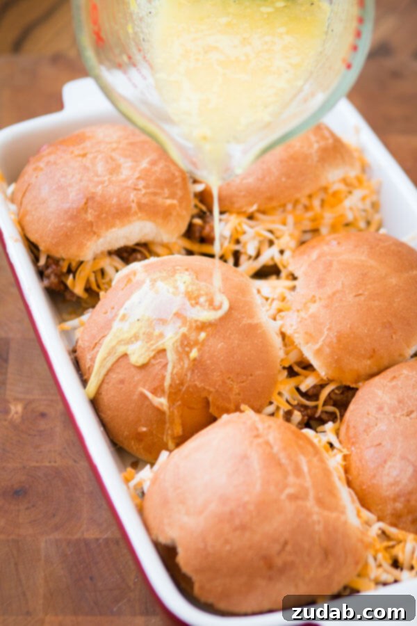 The secret sauce for Cheesy Sloppy Joe Sliders A hand pouring the special butter sauce over the Cheesy Sloppy Joe Sliders before baking.