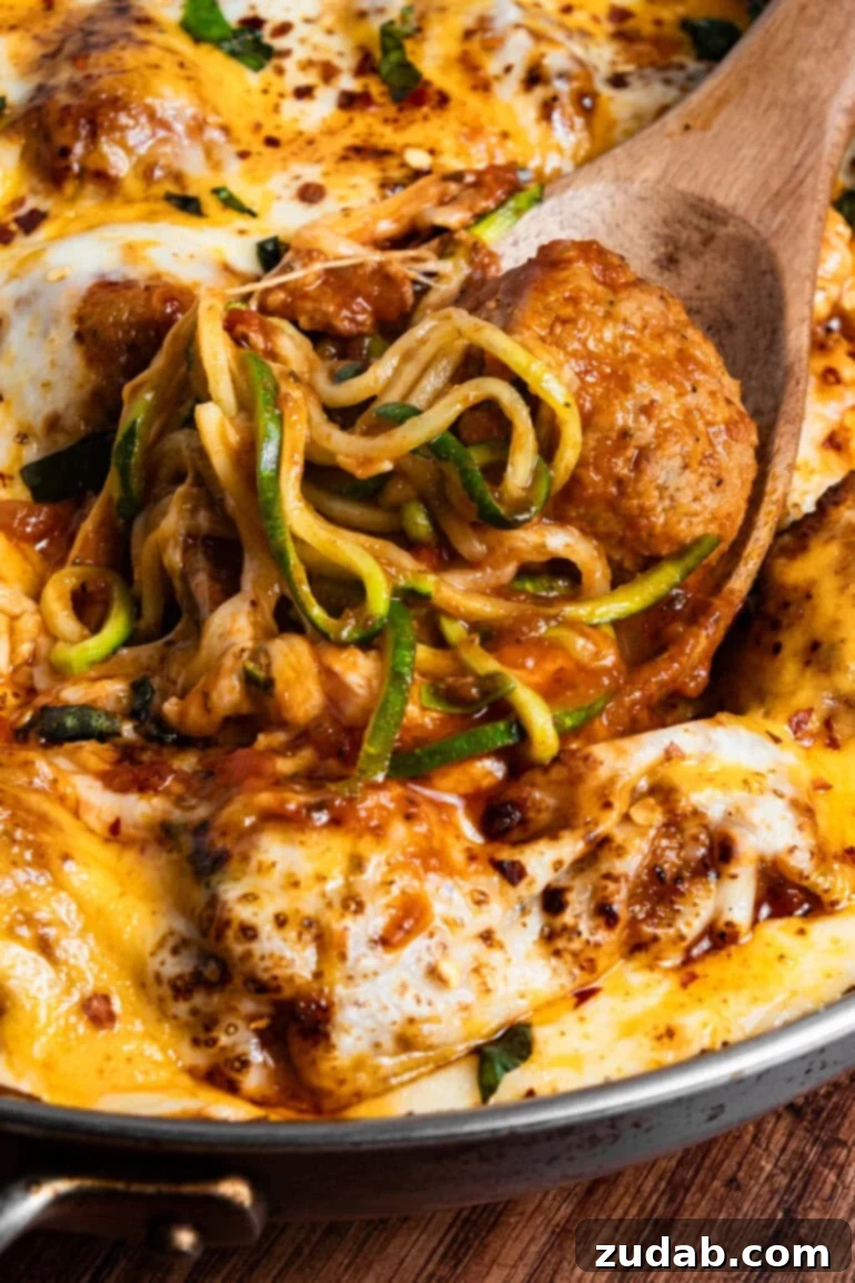 A close-up view of a skillet showcasing perfectly cooked meatballs in a rich marinara sauce, with a fresh pile of bright green zoodles ready to be incorporated, highlighting the key components of the dish.