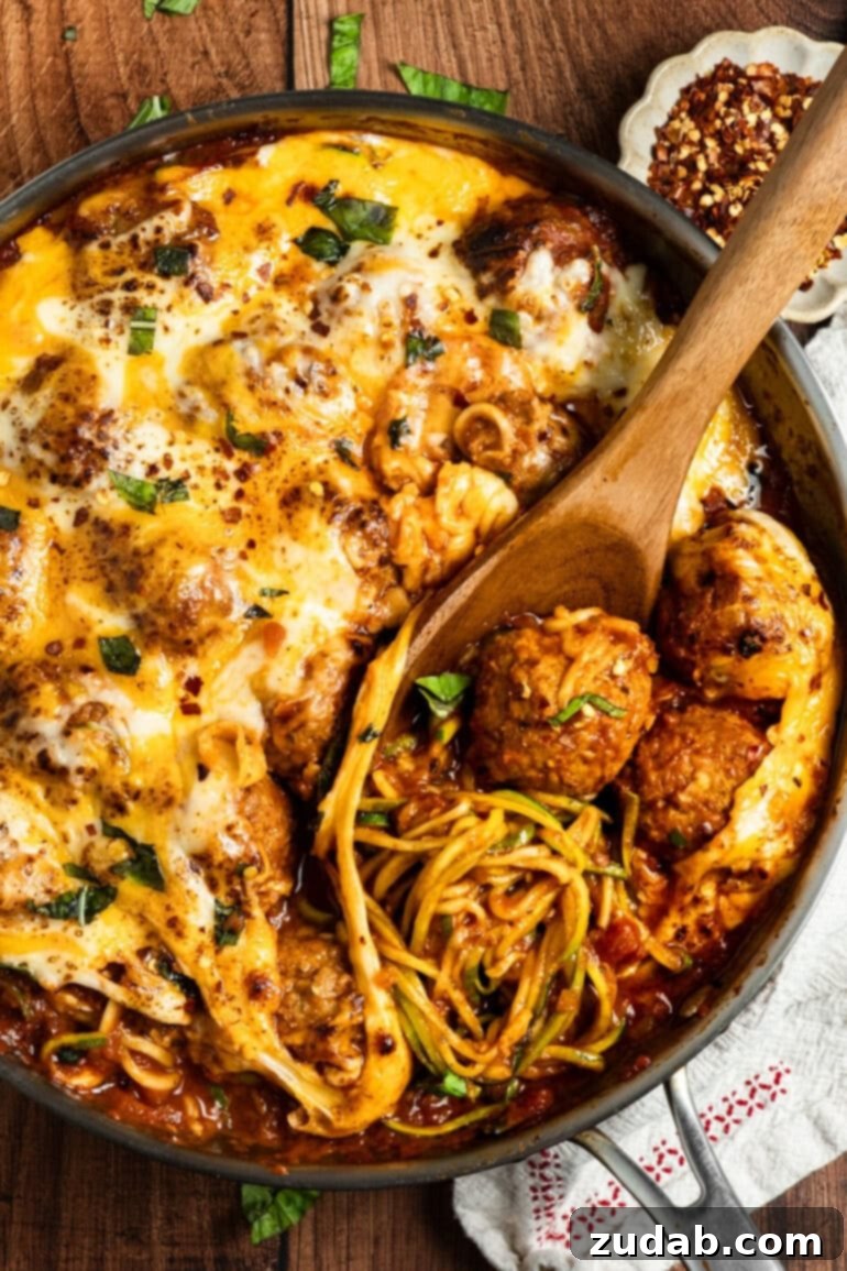 A mouth-watering image of a skillet filled with tender zoodles and meatballs, simmering gently in a vibrant marinara sauce, ready for the final cheesy topping.