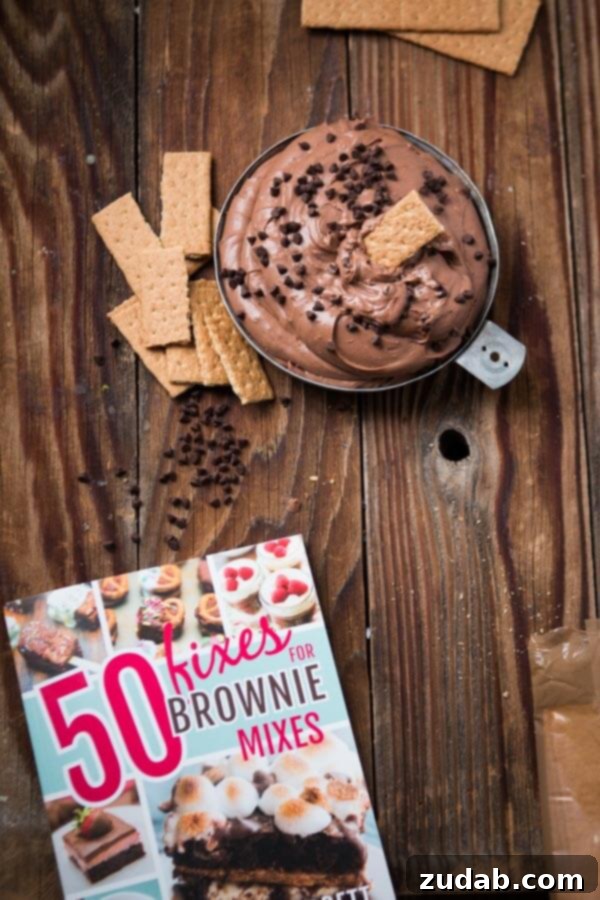 This is your new go-to for appetizers, party food, easy dips, and treat for the holidays. It takes no time to make Brownie Batter Dip! A bowl of rich chocolate brownie dip resting beside an open cookbook, hinting at sweet culinary adventures.