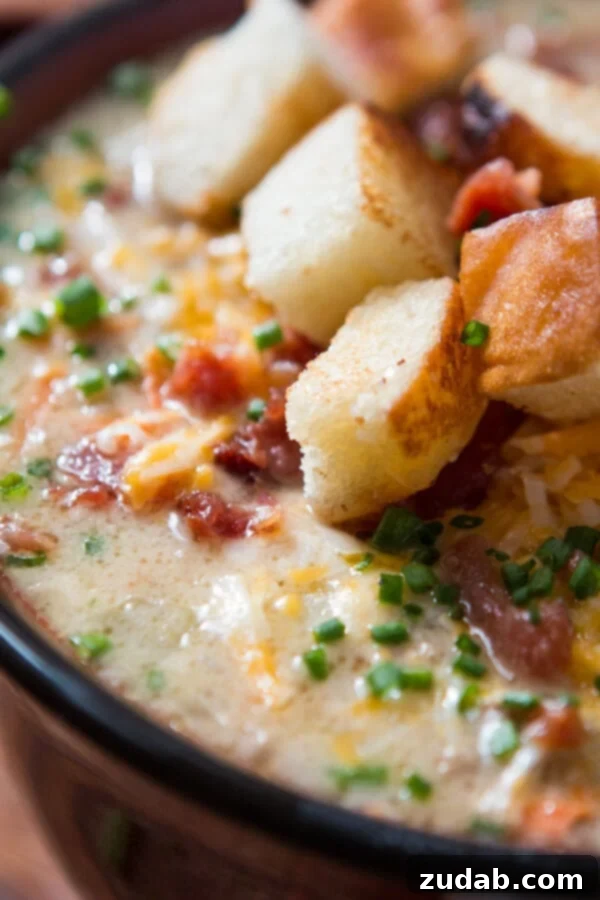 A rich cheeseburger soup garnished with vibrant chives, crisp bacon crumbles, shredded cheddar cheese, and homemade croutons.
