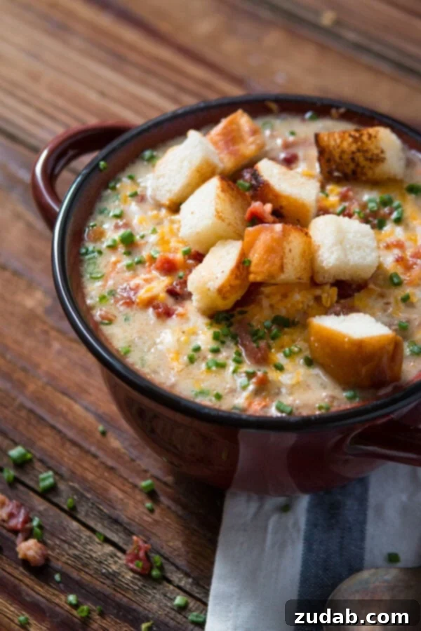 A dark bowl of hearty bacon cheeseburger soup, generously topped with crispy croutons and freshly chopped chives.