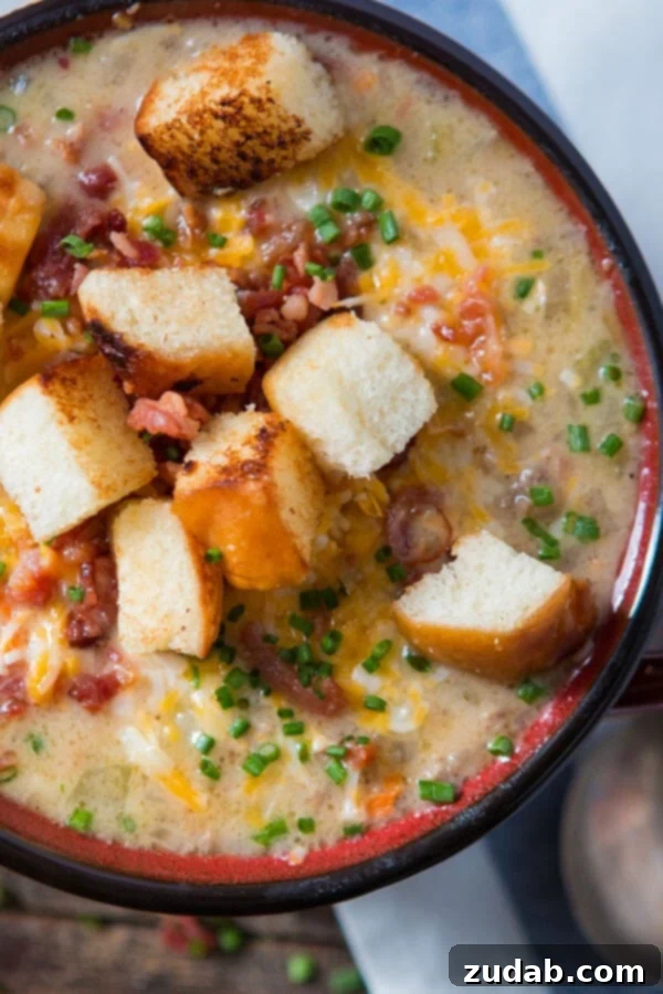 A hearty bowl of cheeseburger soup, lavishly garnished with fresh chives, crunchy croutons, and a generous sprinkle of shredded cheese.