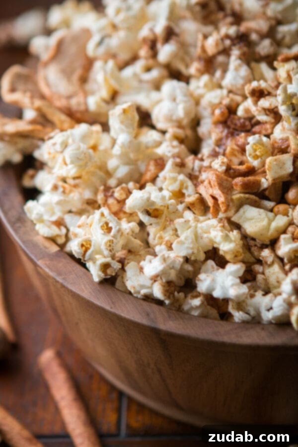 Indulge in a bowl of homemade Easy Apple Pie Popcorn. A hand reaching into a large bowl of Easy Apple Pie Popcorn, highlighting the crispy texture. ohsweetbasil.com