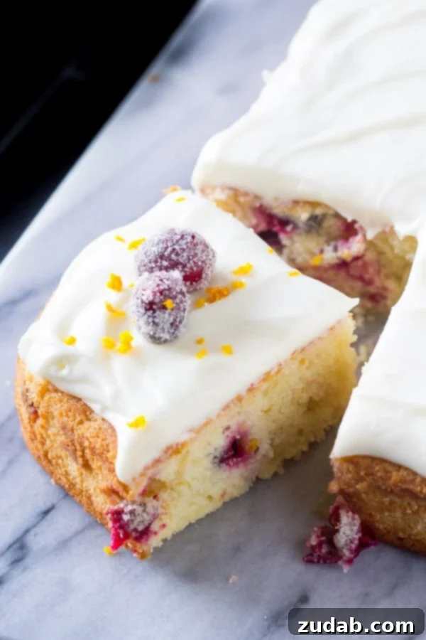 Vibrant Cranberry Orange Cake with Cream Cheese Frosting 3 A corner slice has been cut from a beautiful orange cranberry cake, revealing its moist crumb and topped with luscious cream cheese frosting, sugared cranberries, and a sprinkle of orange zest.