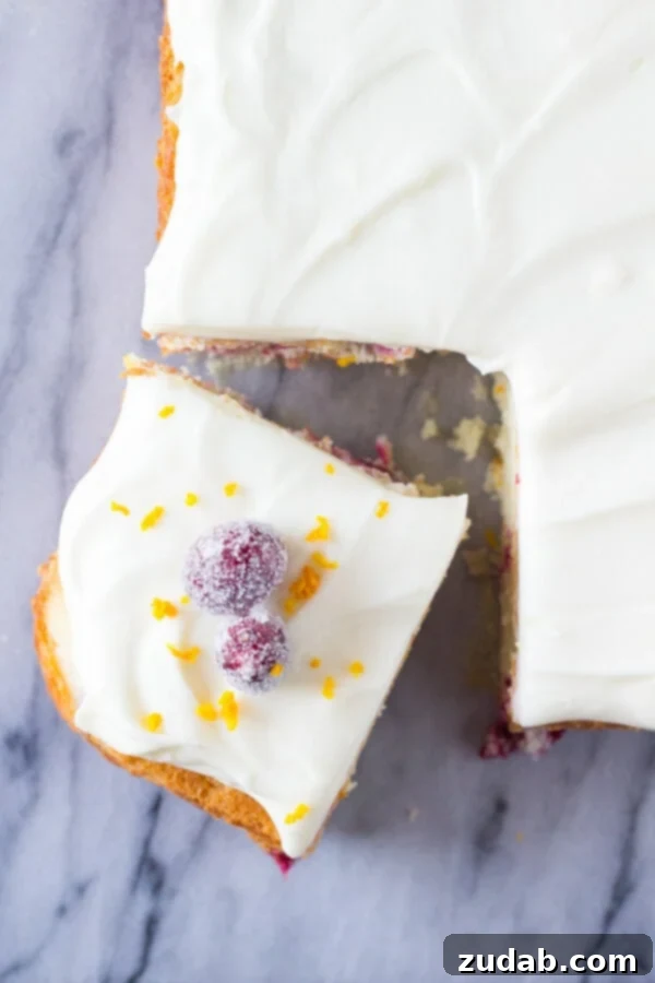 Vibrant Cranberry Orange Cake with Cream Cheese Frosting 4 An overhead shot of a cranberry orange cake with a piece cut out, showcasing its fluffy texture and topped with sugared cranberries and orange zest, ready to be enjoyed as a festive dessert.