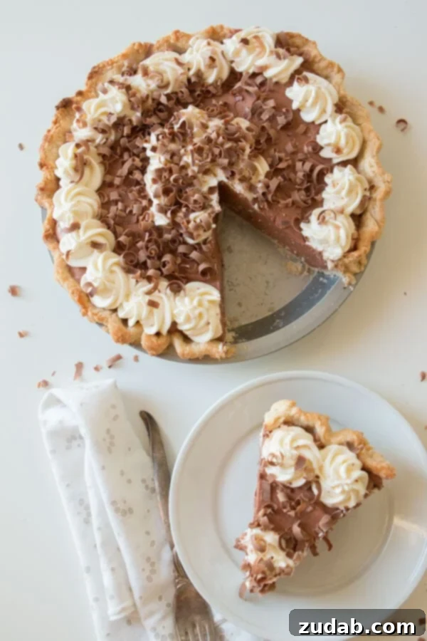 Prepare and serve the perfect Jell-O pudding pie, ideal for quick and delightful dessert moments. A Jell-O pudding pie in its plate with a serving slice removed, placed on a white plate next to it, illustrating its readiness for dessert.