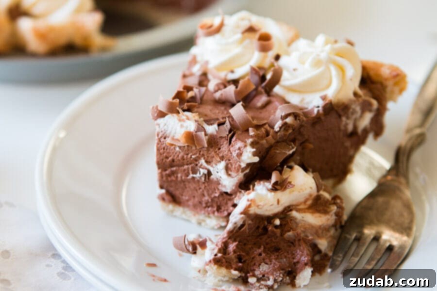 Enjoy a convenient and easy chocolate pie, perfect for any dessert craving. A delectable slice of easy chocolate pie on a white plate, served with a fork, emphasizing its ready-to-eat appeal.